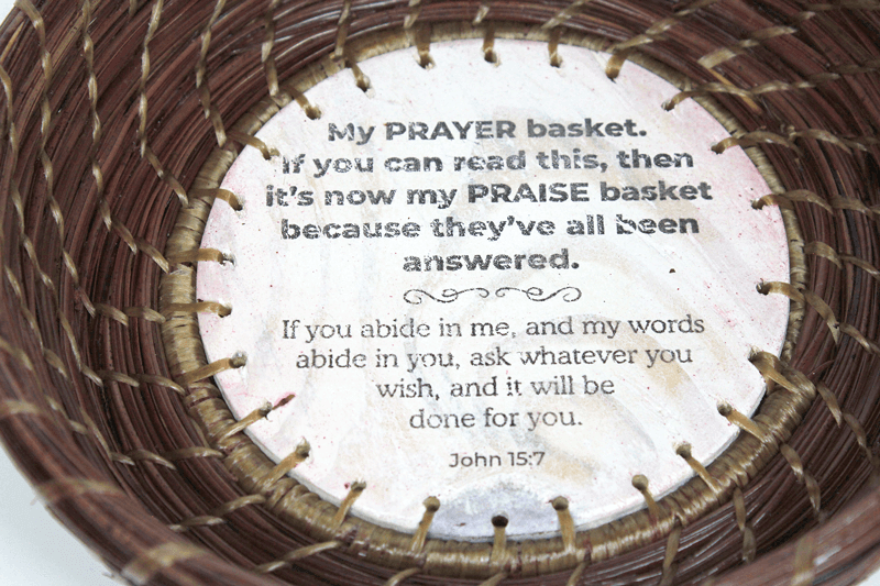 Detail Image of a hand-woven pine straw basket by Patti Jones featuring a hand-made base with writing by Stephen Rountree and a Scripture from John 15:7