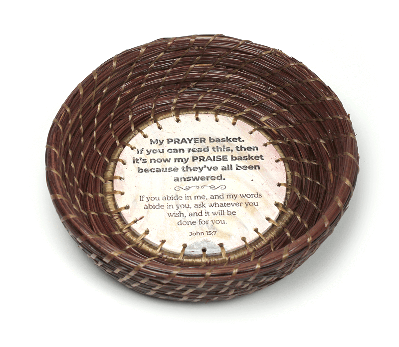 Image of a hand-woven pine straw basket by Patti Jones featuring a hand-made base with writing by Stephen Rountree and a Scripture from John 15:7